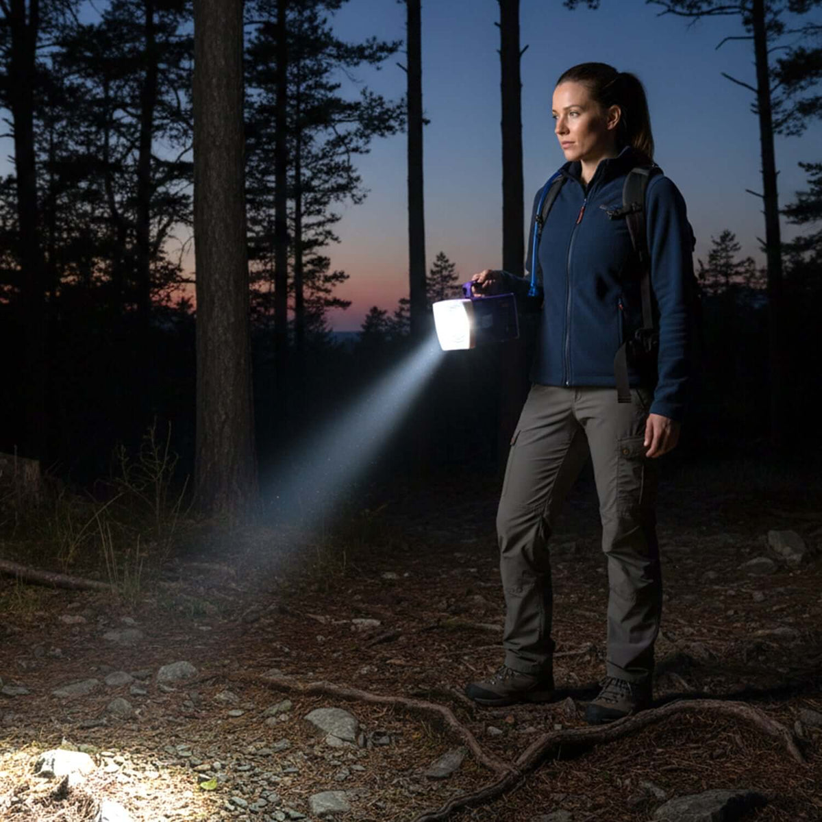 Woman using a rechargeable LED laser torch in a dark forest, showcasing its powerful beam and portability.