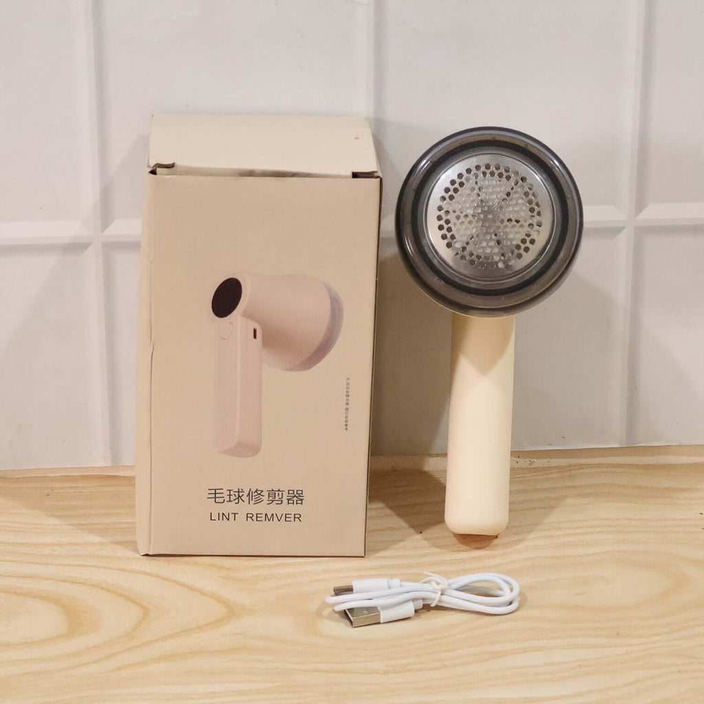 Rechargeable Lint Remover for Clothes placed next to its packaging and USB charging cable.