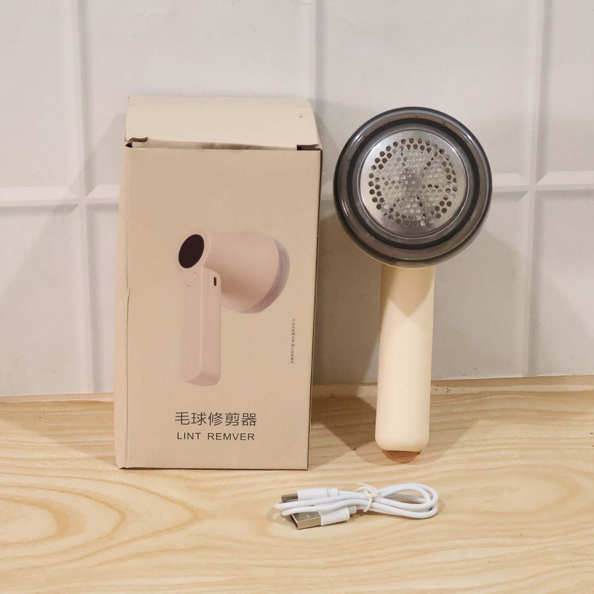 Rechargeable Lint Remover for Clothes placed next to its packaging and USB charging cable.
