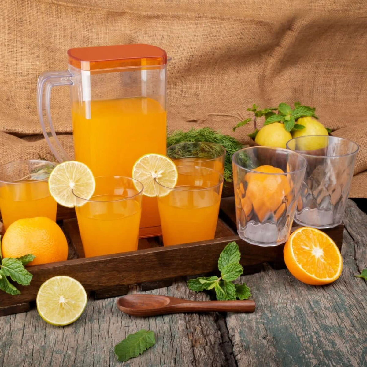 Heat-resistant glass jug set with orange juice, lemon slices, and matching glasses on a wooden tray.