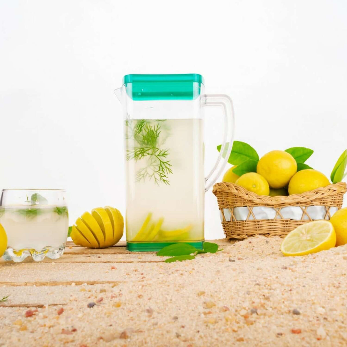 Heat-resistant glass jug set with fresh lemon-infused water, accompanied by lemon slices and a woven basket of lemons.