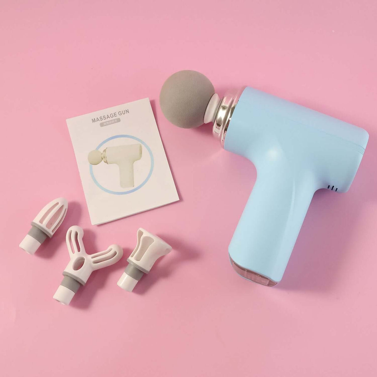 Electric Massage Gun with Interchangeable Heads, featuring multiple interchangeable heads and user manual on pink background.