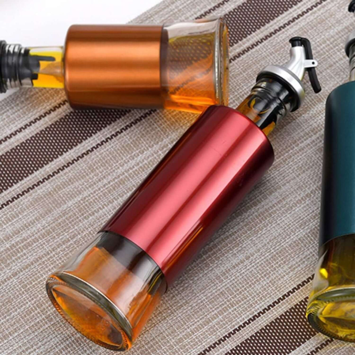 Glass oil vinegar dispenser bottle with varied colored spouts on textured fabric background.