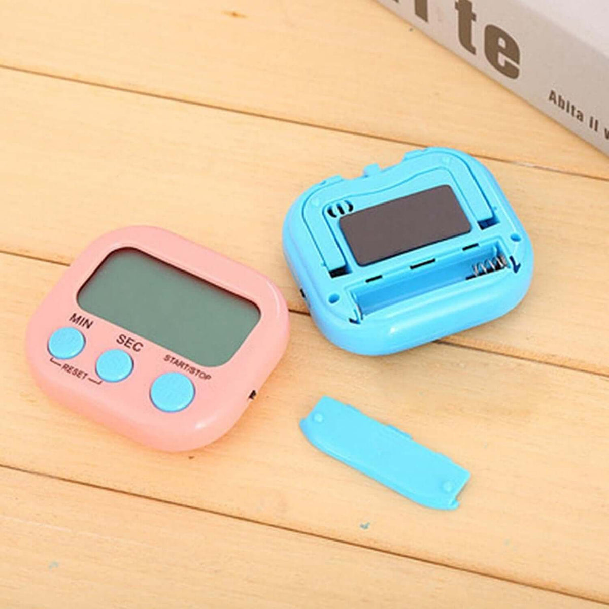 Digital kitchen timer big digits in pink and blue colors on a wooden surface, featuring buttons and battery compartment.