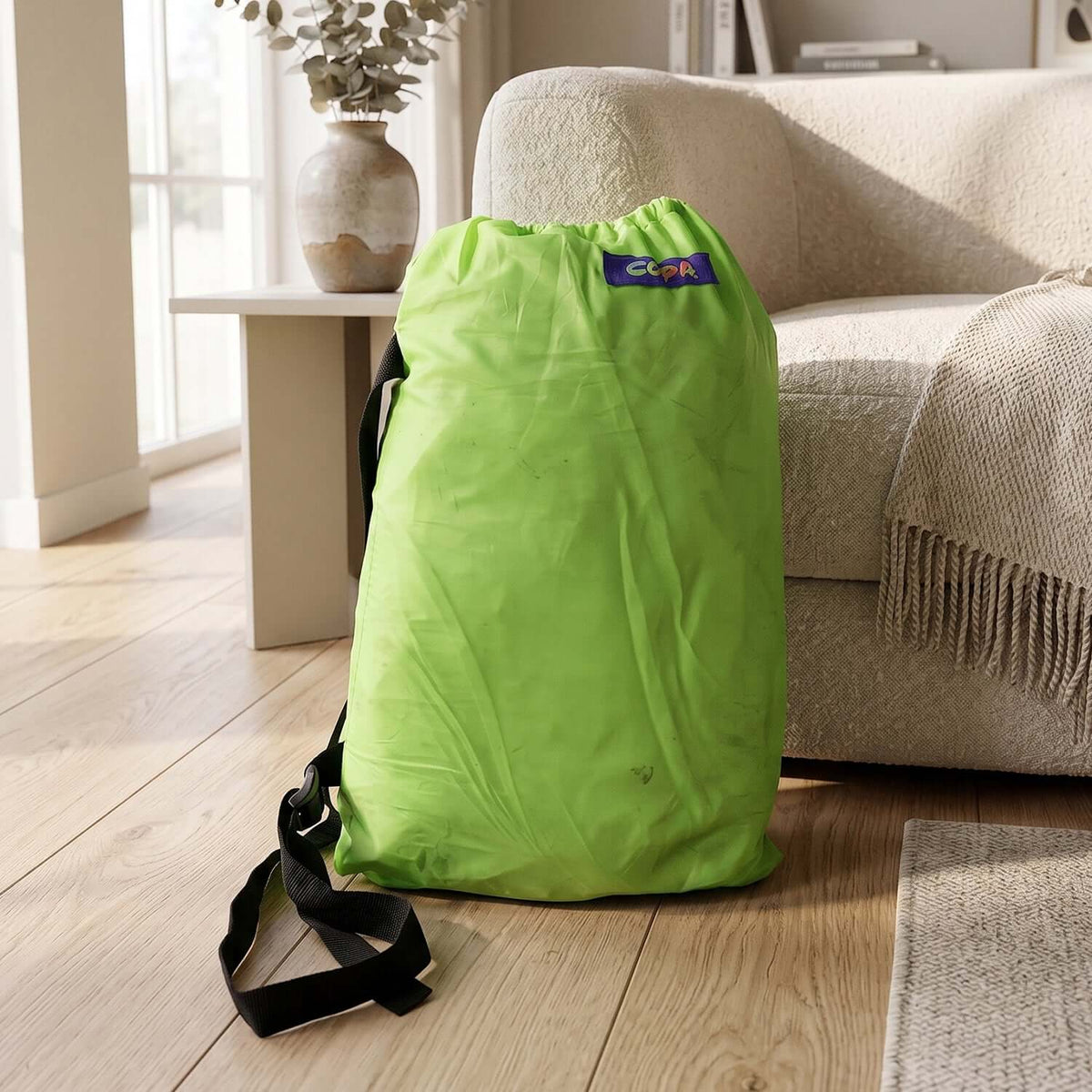 Inflatable air lounger for outdoor use carry bag in bright green resting beside a couch.