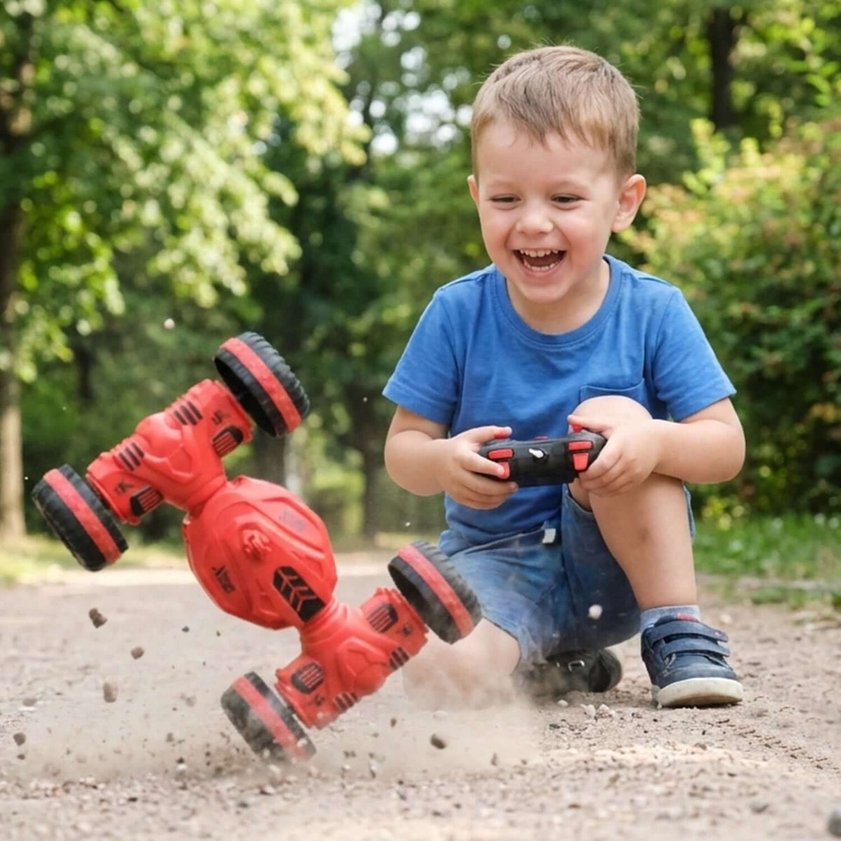 Boy playing with a remote control deformation stunt car that is spinning on dirt path outdoors.