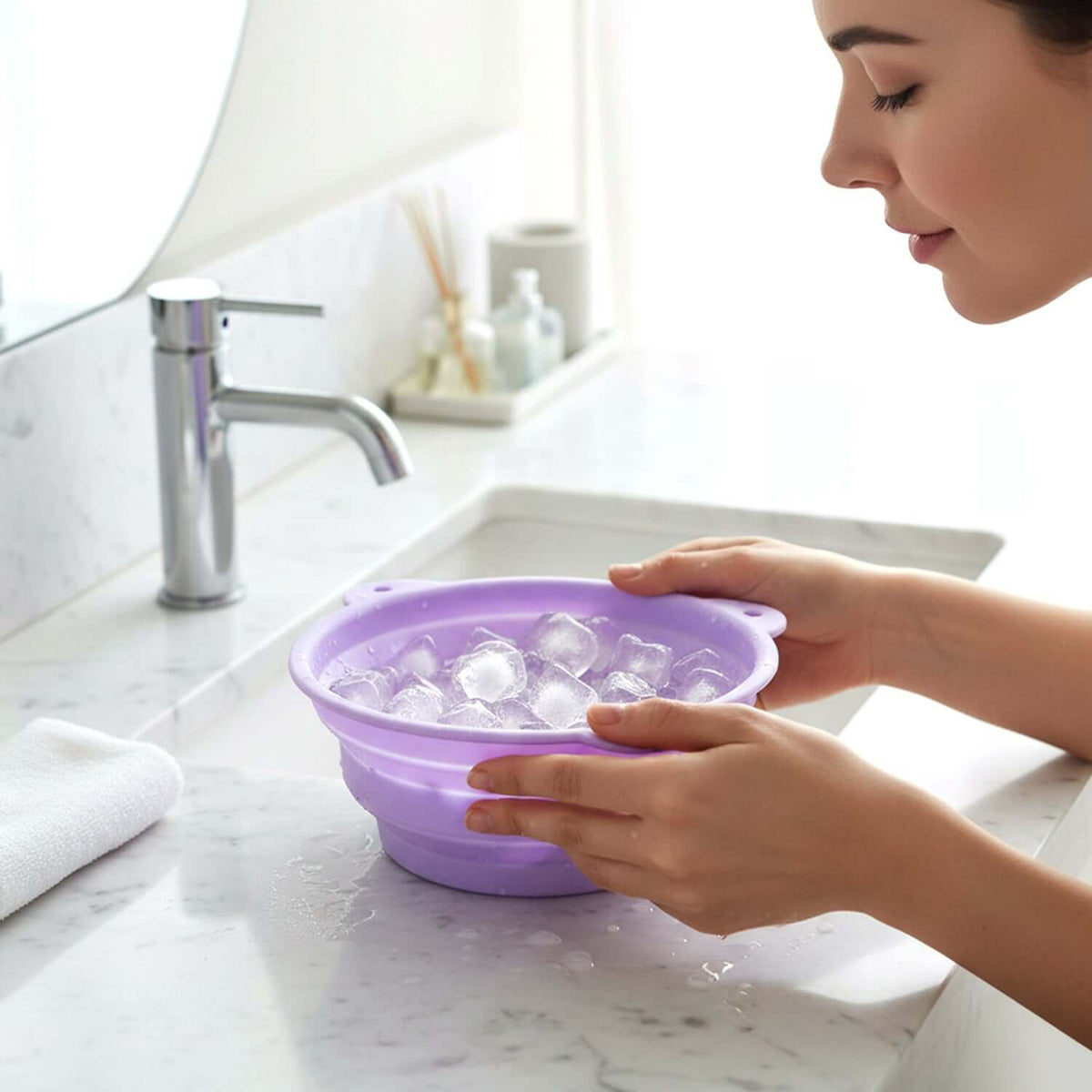 A user holds a collapsible silicone facial ice bath bowl filled with ice cubes near a sink.